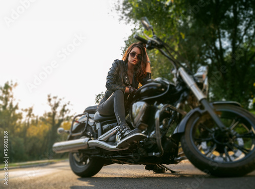 Amazing powerful girl sitting on vintage motorcycle parked on the road and looking seriously at camera 