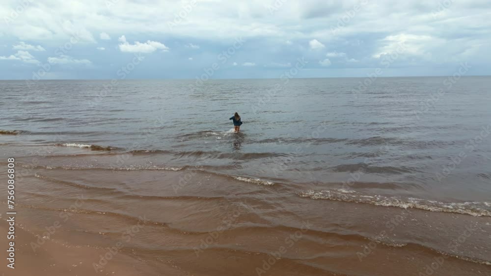 Coastal charm: Aerial shot reveals the natural beauty as a woman walks along a sandy beach near the ocean Coastal charm: Aerial shot reveals the natural beauty as a woman walks along a sandy beach near the ocean