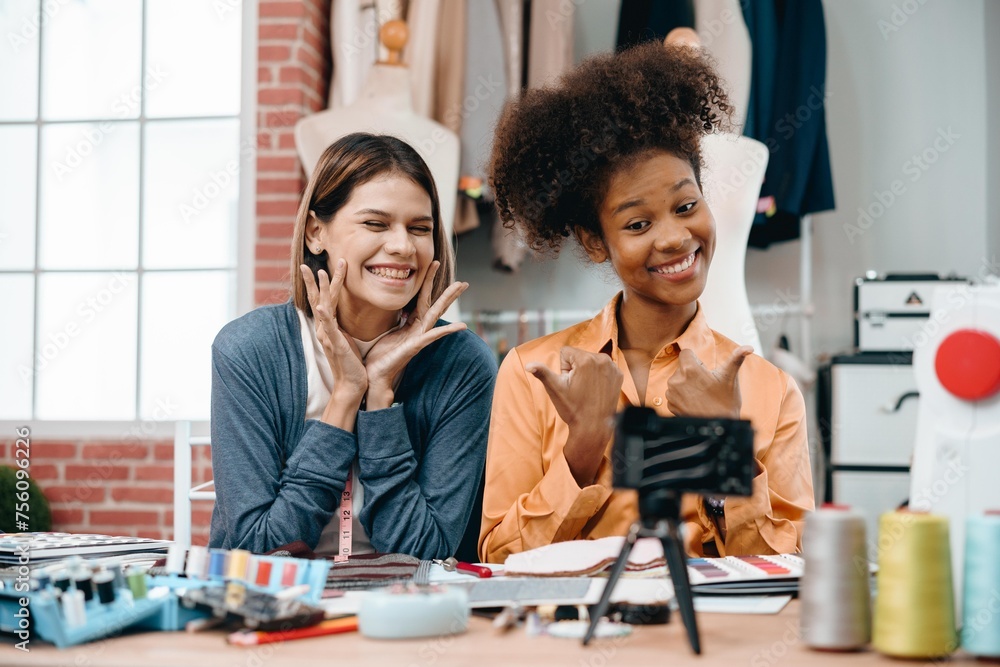 Two women are smiling and waving at the camera. They are sitting at a desk with online live to sale the product. Scene is friendly and lighthearted Two women are smiling and waving at the camera. They are sitting at a desk with online live to sale the product. Scene is friendly and lighthearted
