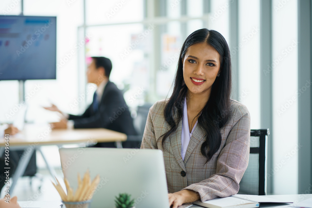 Happy young confident businesswoman sitting at the office table with group of colleagues Happy young confident businesswoman sitting at the office table with group of colleagues
