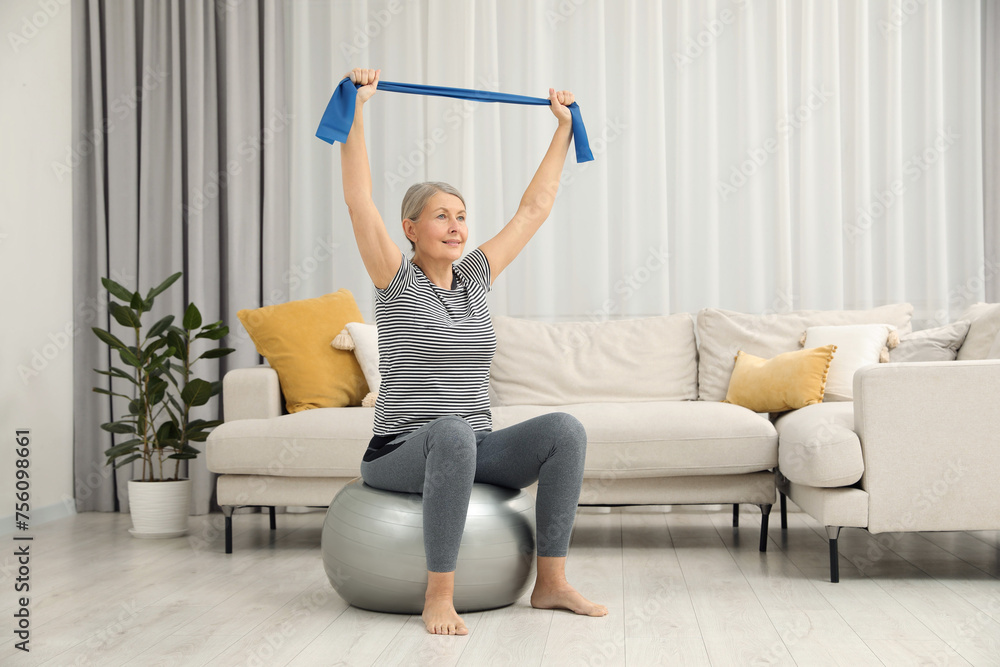 Senior woman doing exercise with elastic resistance band on fitness ball at home Senior woman doing exercise with elastic resistance band on fitness ball at home