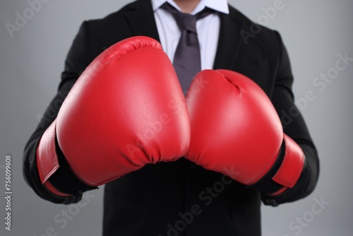 Businessman in suit wearing boxing gloves on grey background, closeup © New Africa