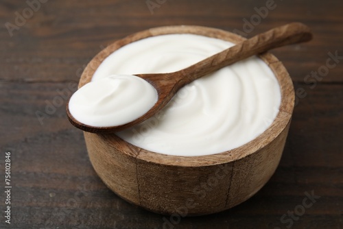 Delicious natural yogurt in bowl and spoon on wooden table, closeup
