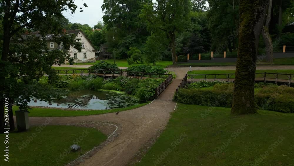 A bridge crosses the pond in the park, surrounded by trees and grass A bridge crosses the pond in the park, surrounded by trees and grass