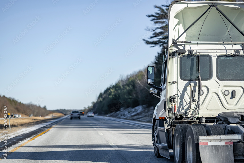 Day cab white big rig semi truck tractor with roof spoiler and without semi trailer driving on the winter divided highway road in New England