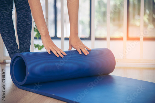 Woman hands rolled up yoga mat on gym floor in yoga fitness training room. Home workout woman close up hands rolling foam yoga gym mat. Woman barefoot home workout sportive healthy lifestyle concept