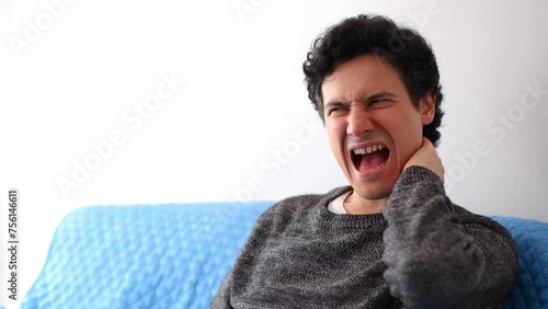 Latin man with tousled black hair has severe neck pain which he massages to relieve the pain, horizontal video