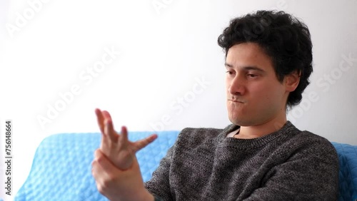 Latin man with messy black hair performs hand exercises to relieve severe pain that overwhelms him, horizontal video
