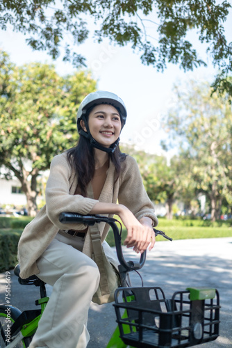 Young beautiful Asian woman in safe bike helmet and protective exercises in riding using electric bicycle in a city park