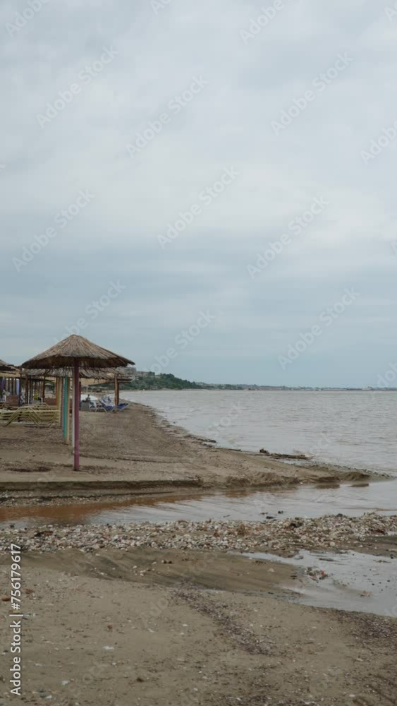 Vertical view of destroyed and washed out sea coast after passage of storm. Empty beach of tourist resort with sun umbrellas. Cloudy and cold weather during passage of cold front, no people. Vertical view of destroyed and washed out sea coast after passage of storm. Empty beach of tourist resort with sun umbrellas. Cloudy and cold weather during passage of cold front, no people.