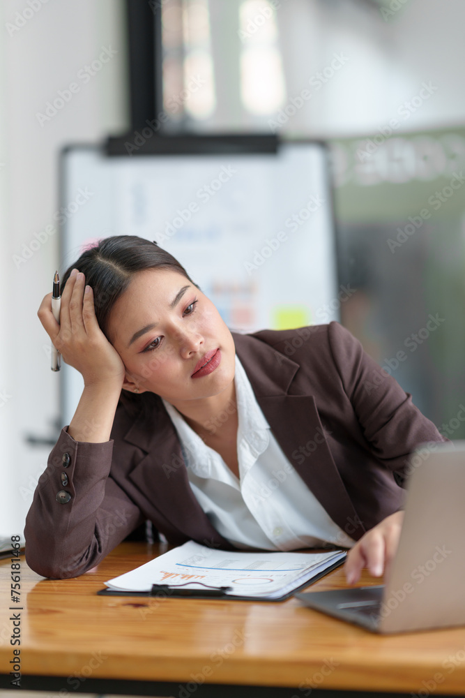 Asian businesswoman who is tired has a headache, is stressed, sleepy, angry, and bored from sitting at a desk for a long time doing contact work. online business on laptop Office syndrome concept. Asian businesswoman who is tired has a headache, is stressed, sleepy, angry, and bored from sitting at a desk for a long time doing contact work. online business on laptop Office syndrome concept.