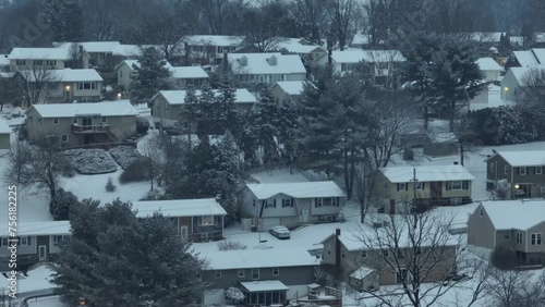 Snowy grey day in american suburb. Houses located on hill snow covered. Leafless trees in rural area. Aerial zoom wide shot.