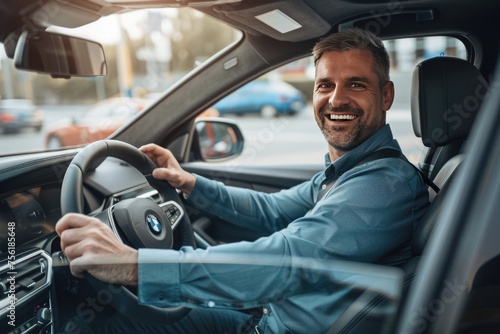 Handsome young man is driving a car and smiling. He is sitting on the steering wheel and looking at camera