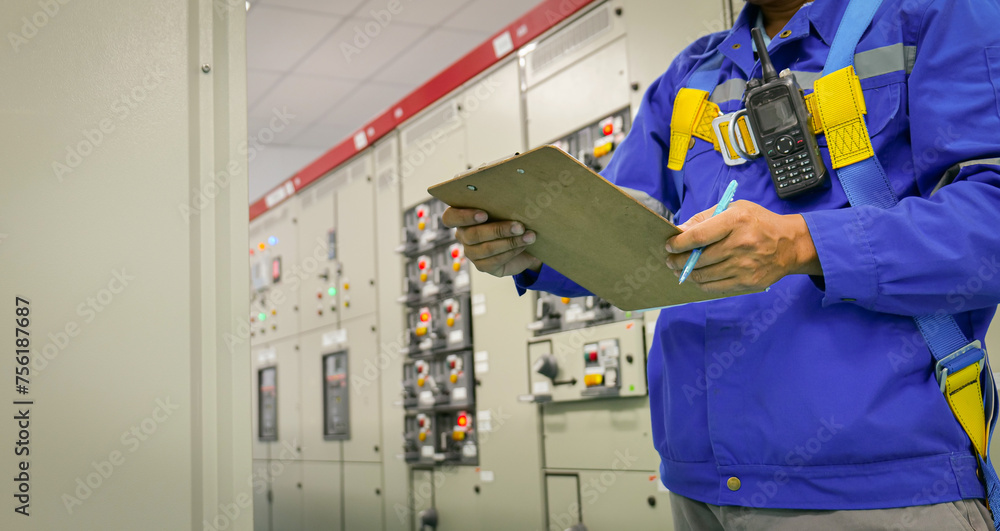 A man in a blue jacket is writing on a clipboard in front of a row of electrical A man in a blue jacket is writing on a clipboard in front of a row of electrical