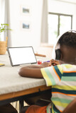 African American boy with headphones uses a tablet with a blank screen at a table with copy space