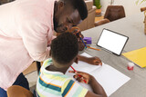 African American father assists a young son with homework at a table with copy space