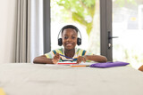 African American boy with headphones smiles while studying at home in an online class