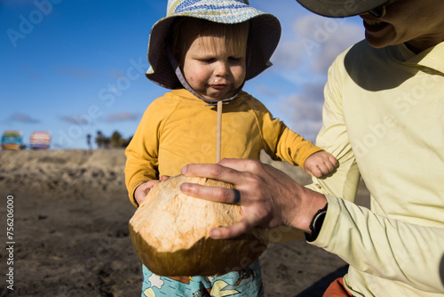 A young boy drinks water from a fresh coconut on the beach.