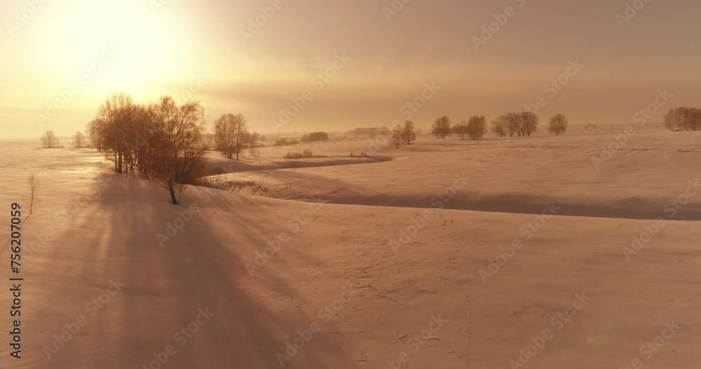 Drone aerial view of cold winter landscape arctic field, trees covered with frost snow, ice river and sun rays over horizon. Extreme low temperature weather. Drone aerial view of cold winter landscape arctic field, trees covered with frost snow, ice river and sun rays over horizon. Extreme low temperature weather.