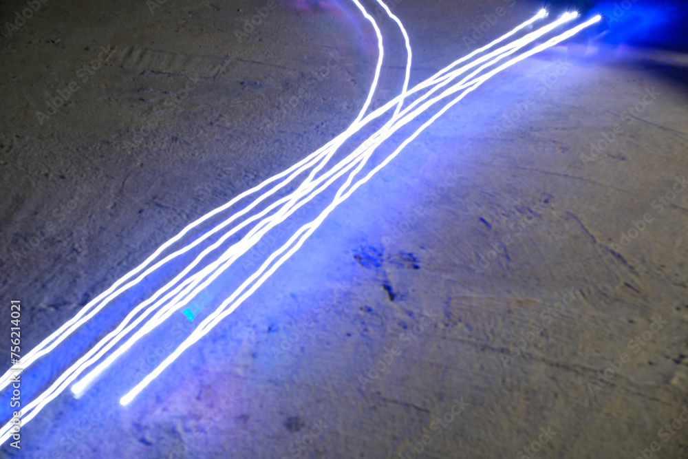 Fototapeta premium Lights Photography. Long Exposure. Light trail in shape of branching lines. Lights from the movement of the RC (Remote Control) Car. Blur Motion. Light trails are white and bright blue. Long Exposure