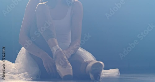 Ballerina gracefully puts on pointe shoes while sitting on the floor. Diffused soft light and smoke photo