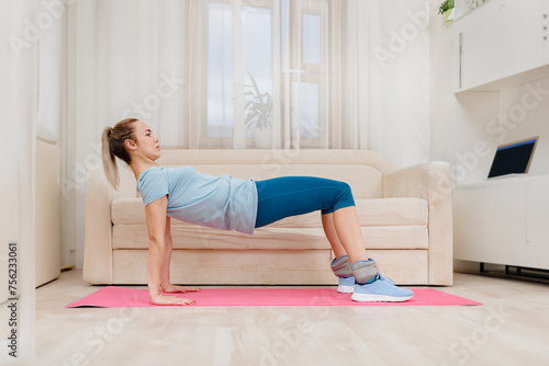 Pretty healthy active woman doing pilates exercise while watching online tutorial on laptop, Home exercise evolution: A girl joins an online course, incorporating the sofa into her workout routine