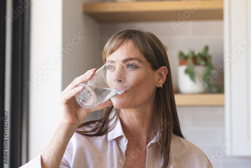 Caucasian woman drinks water in a kitchen