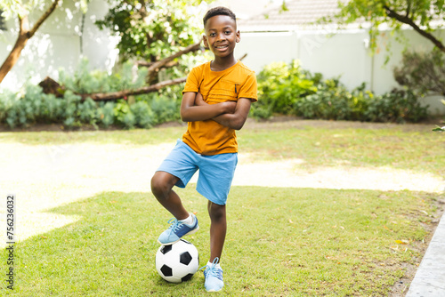 African American boy stands confidently with a soccer ball in a garden photo