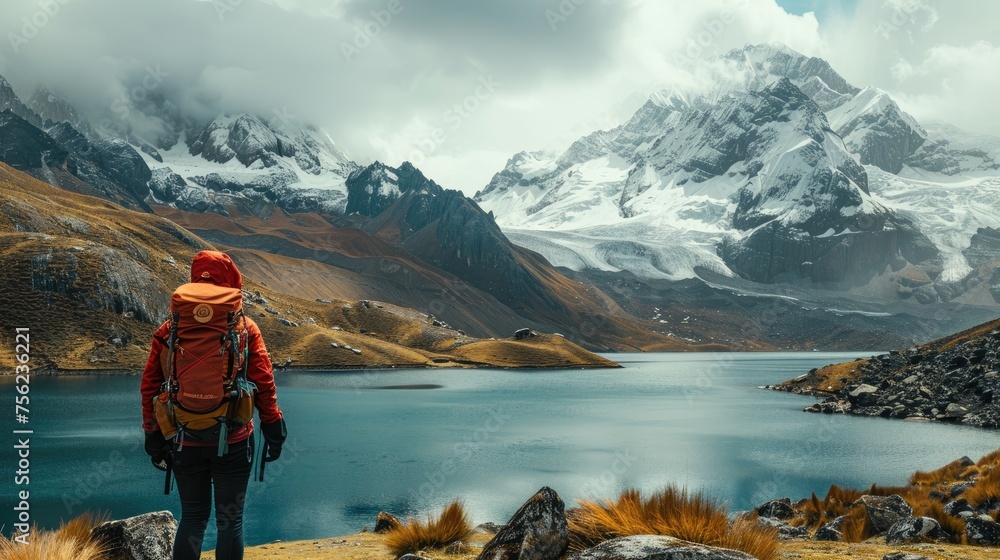 A hiker with a backpack stands before a flowing stream, looking towards the majestic snow-capped mountain peaks in the distance, enveloped by the vastness of the wilderness.