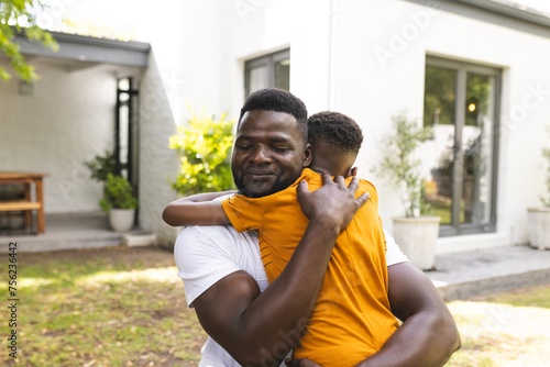 African American father embraces his son in a warm hug outdoors in the backyard photo