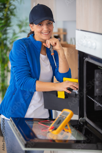 a smiling beautiful woman fixing a small oven photo