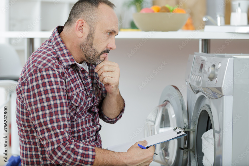 thinking plumber with clipboard near washing machine thinking plumber with clipboard near washing machine