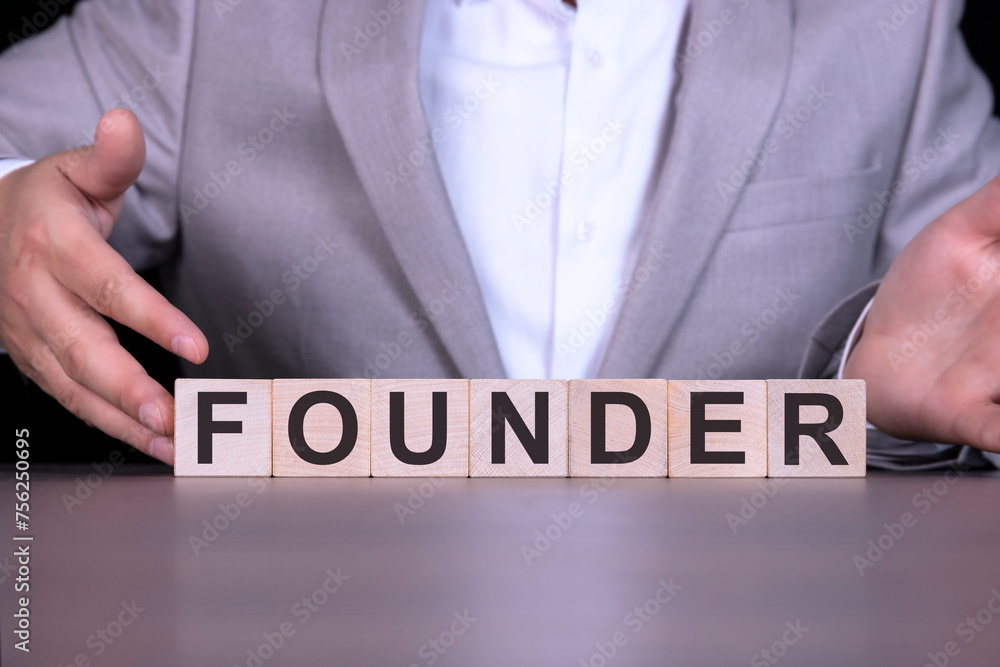 FOUNDER, the word is written on wooden cubes, blocks on the background of a man, a businessman in a gray suit. FOUNDER, the word is written on wooden cubes, blocks on the background of a man, a businessman in a gray suit.