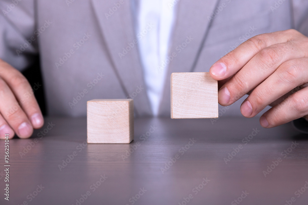 A businessman holds two wooden cubes with empty space for icons, free space for letters, numbers, symbols or labels. A businessman holds two wooden cubes with empty space for icons, free space for letters, numbers, symbols or labels.