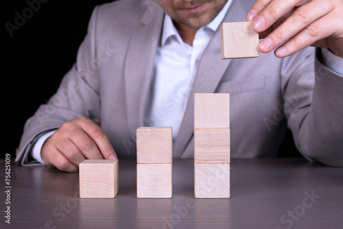 Growth or business concept on wooden cubes against the background of a businessman in a gray suit sitting at the table. Copy space. © Iryna