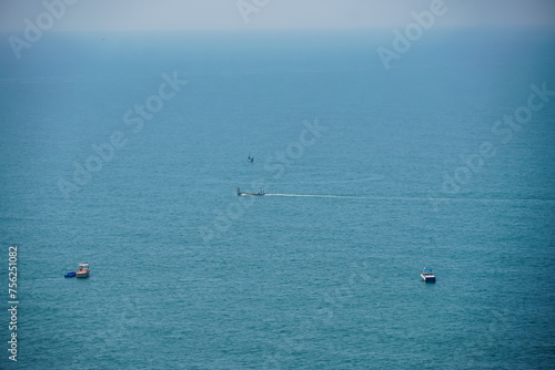 AERIAL: Fishing boat leaves a trail in the calm ocean water as it speeds towards endless horizon on a picturesque summer day. Four boats can be seen into the vast open ocean. White boats in blue water © deepshikha