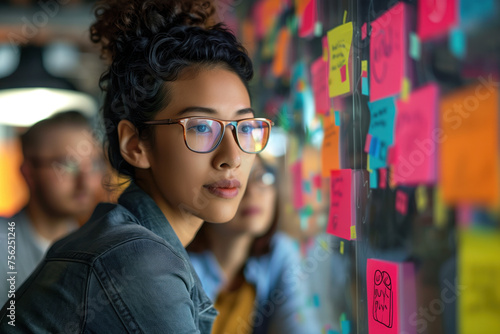 Portrait of a woman in glasses standing in front of a wall covered with colored post-it notes. A slide background for showcasing the brainstorming process. Created with Generative AI technology.