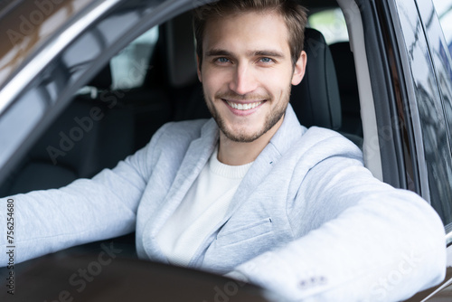 Car leasing, buying, retail, renting concept. Portrait of happy guy in casual outfit getting into new auto, placing hand on wheel, cheerfully smiling at camera.