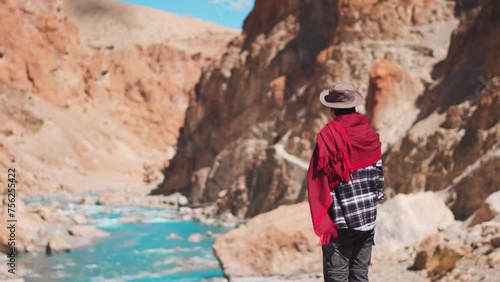 Rear view shot of an Indian man wearing hat and shawl looking at the blue Tsarap Chu river on the way towards Phugtal Monastery in remote area of Zanskar Valley in Ladakh, India. Tourist in Himalayas. photo