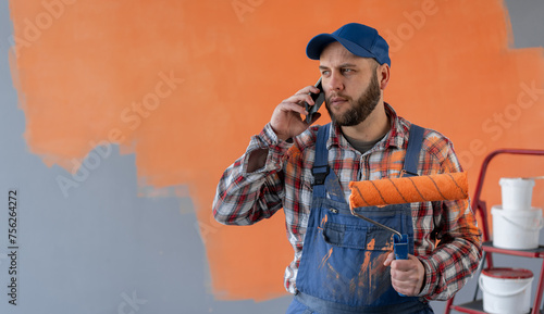 Bild auf Leinwand house painter man calling on mobile phone, holding paint roller, making home ren
