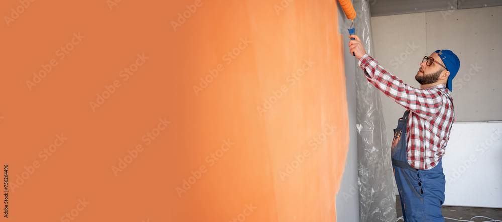 Side view of painter man painting the wall, with paint roller on big empty space. Copy space - obrazy, fototapety, plakaty 