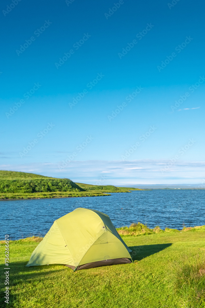 Cover page with a lonely green tent pitched at Myvatn lake shore at sunny day and blue sky with copy space, at central camping site