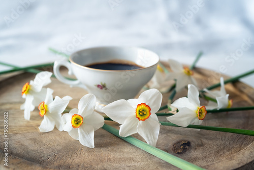 Still life with a delicate decoration of white daffodil flowers around a baroque fine porcelain coffee cup on a wooden tray © Jess_Ivanova