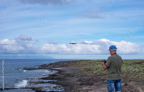Rear view of active man guiding drone flight along sea coast. People and weekend tourism, leisure and outdoor activity lifestyle. Ocean and southern coast of Tenerife, Punta Rasca natural park