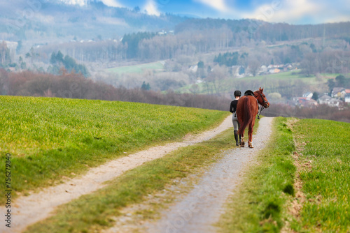 Rider walks her horse along a field path, landscape image in landscape format.