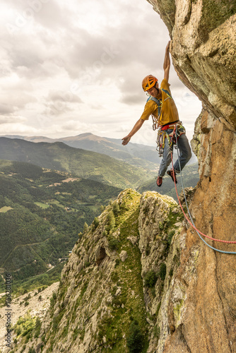 A man is climbing a rock wall with a yellow shirt and an orange helmet. Concept of adventure and excitement, as the man is taking on a challenging and thrilling activity