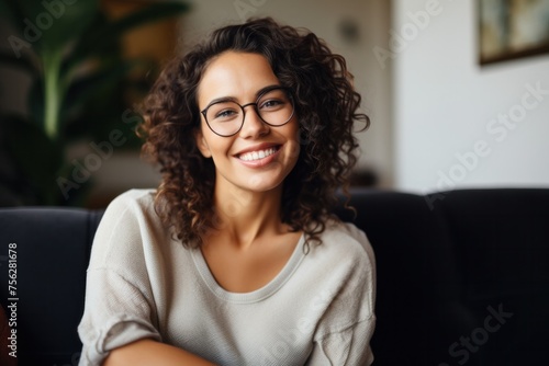 Smiling young woman wearing casual clothes and glasses sitting relaxed on sofa