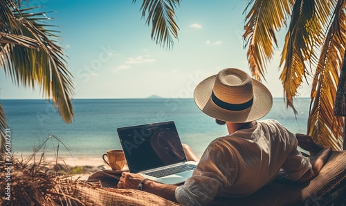 A man wearing a straw hat working on a laptop while sitting on a hammock by the ocean, representing a remote working lifestyle