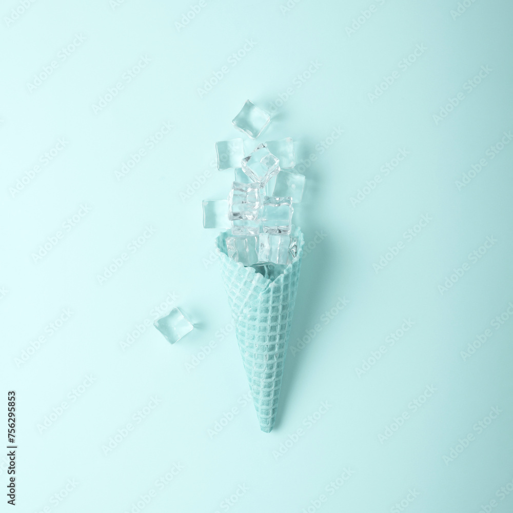 Ice cream cone with ice cubes on light blue background, top view. Summer minimalist concept.