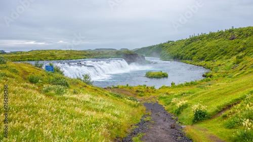 Panoramic with Faxafoss waterfall with dramatic sky and green hills. Beautiful Icelandic landscape, huge cliff, water cascade and rock in moss